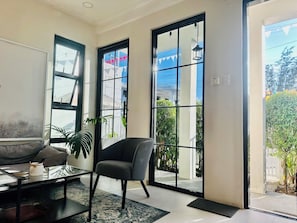 Una sala moderna con sofá, sillón, mesa de centro de vidrio y un ventanal con vistas al exterior.