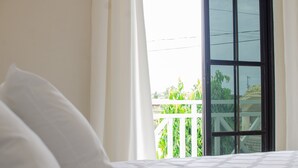 A hotel room with a bed, white curtains, and a balcony with a white railing.
