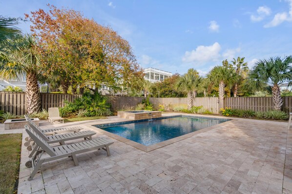 A backyard with a swimming pool, lounge chairs, and a wooden fence.