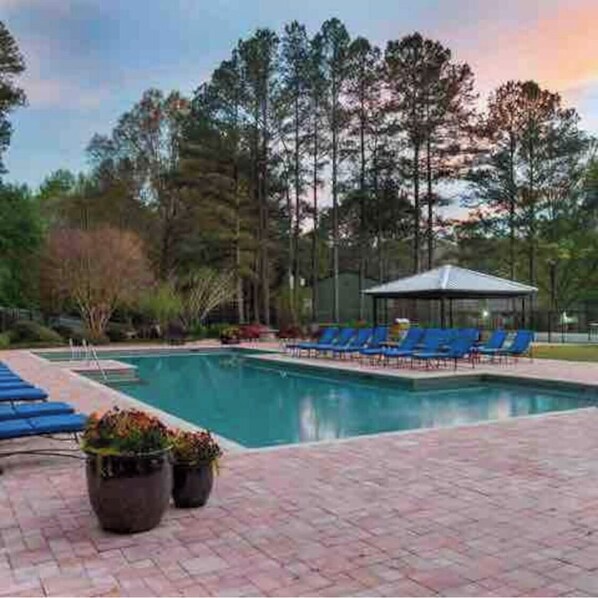 Relax by the serene pool surrounded by tall trees and a clear sky.