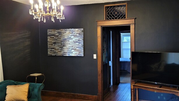 Un salon à l’ambiance sombre, agrémenté d’un lustre, d’un téléviseur à écran plat et d’un élément décoratif mural.