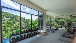 Un gimnasio con amplios ventanales, equipamiento de ejercicio y un banco.