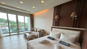 Habitación de hotel con una cama grande, un sofá, una mesita y un balcón con vistas a zonas verdes.