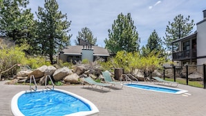 A swimming pool area with two pools, lounge chairs, and a building in the background. - Midtown 1BR, Pool & Spa, Close to Shops 538 (Mammoth Lakes)