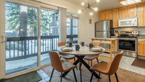 A modern kitchen with wooden cabinets, stainless steel appliances, and a dining area with a round table and four chairs. - Midtown 1BR, Pool & Spa, Close to Shops 538 (Mammoth Lakes)