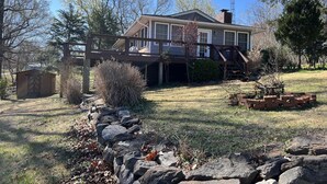 A house with a covered porch, a stone wall, and a small shed. - Charming home with lake views (Boydton)