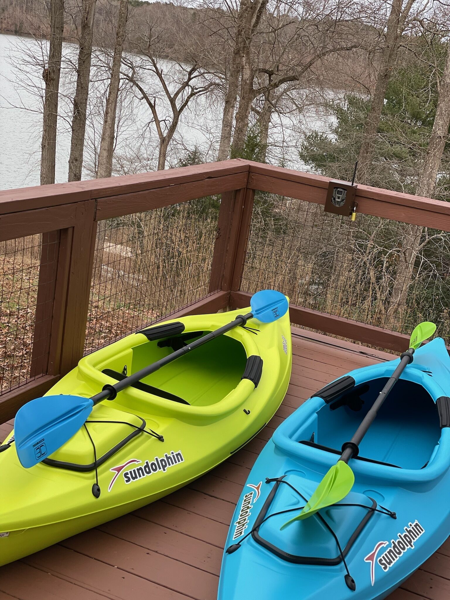 Two kayaks on a wooden deck with a view of a lake and trees.