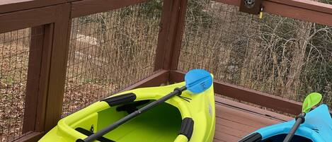 Two kayaks on a wooden deck with a view of a lake and trees.
