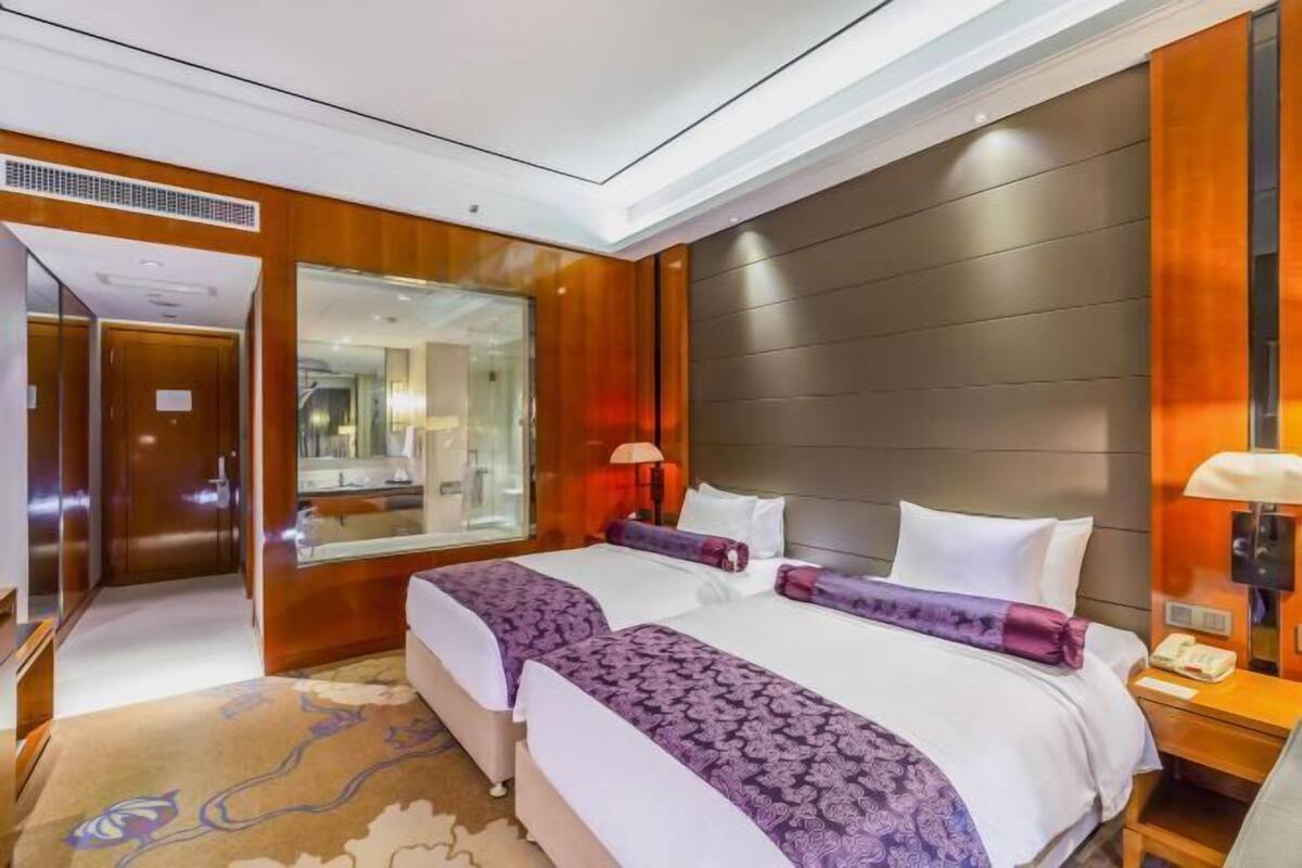 Quarto de hotel com duas camas, um espelho grande, painéis de madeira e uma mesa de cabeceira com abajur.