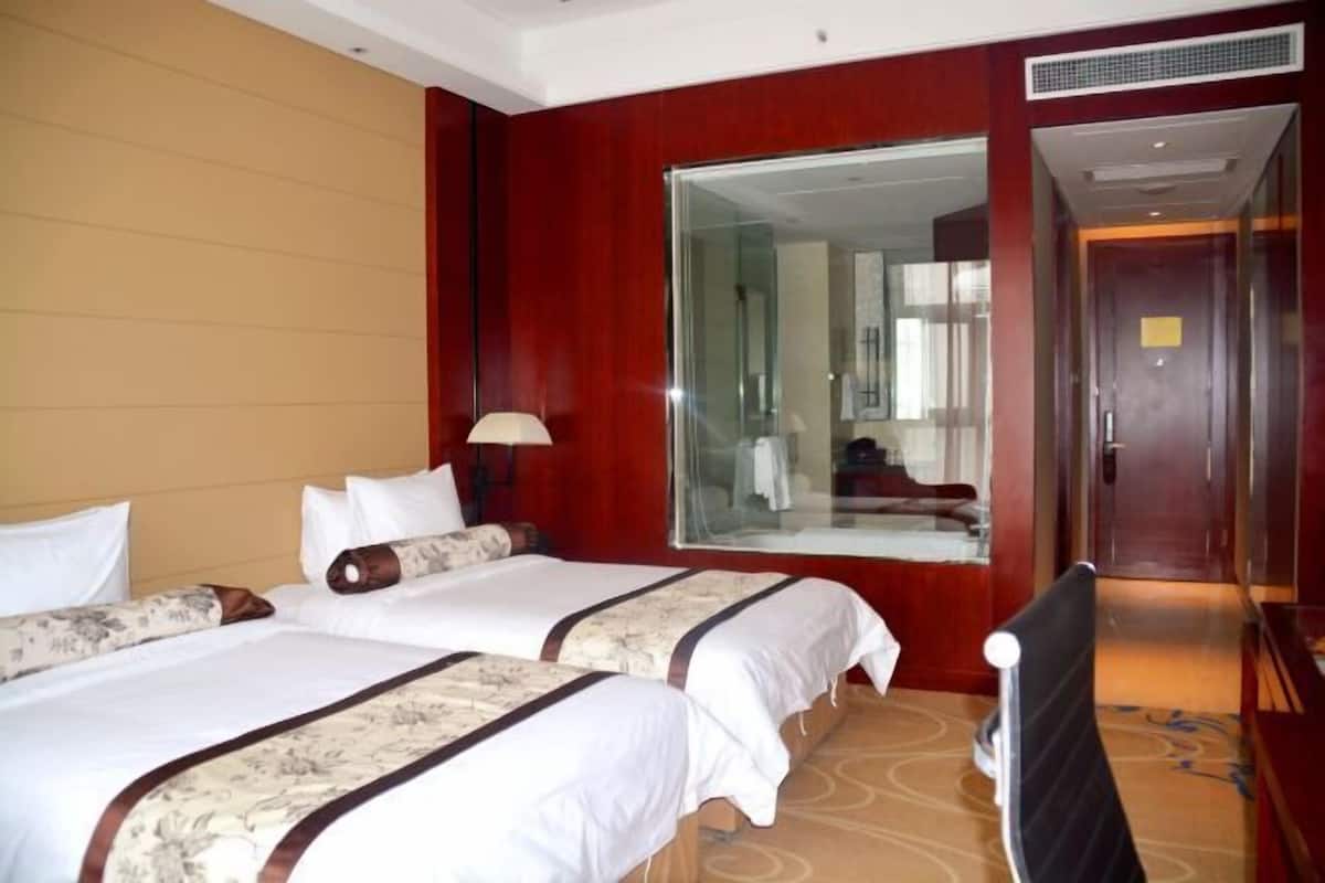 Quarto de hotel com duas camas, um espelho grande, uma mesa e uma cadeira.