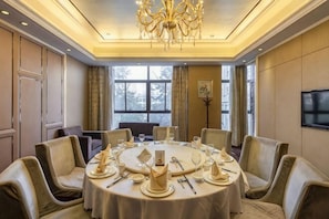 A conference room with a round table set for a meeting, equipped with chairs, a chandelier, and a television on the wall. - Shenghe Regent Hotel (Changge)