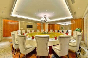 Une salle de conférence avec une table ronde, des chaises blanches et un lustre.