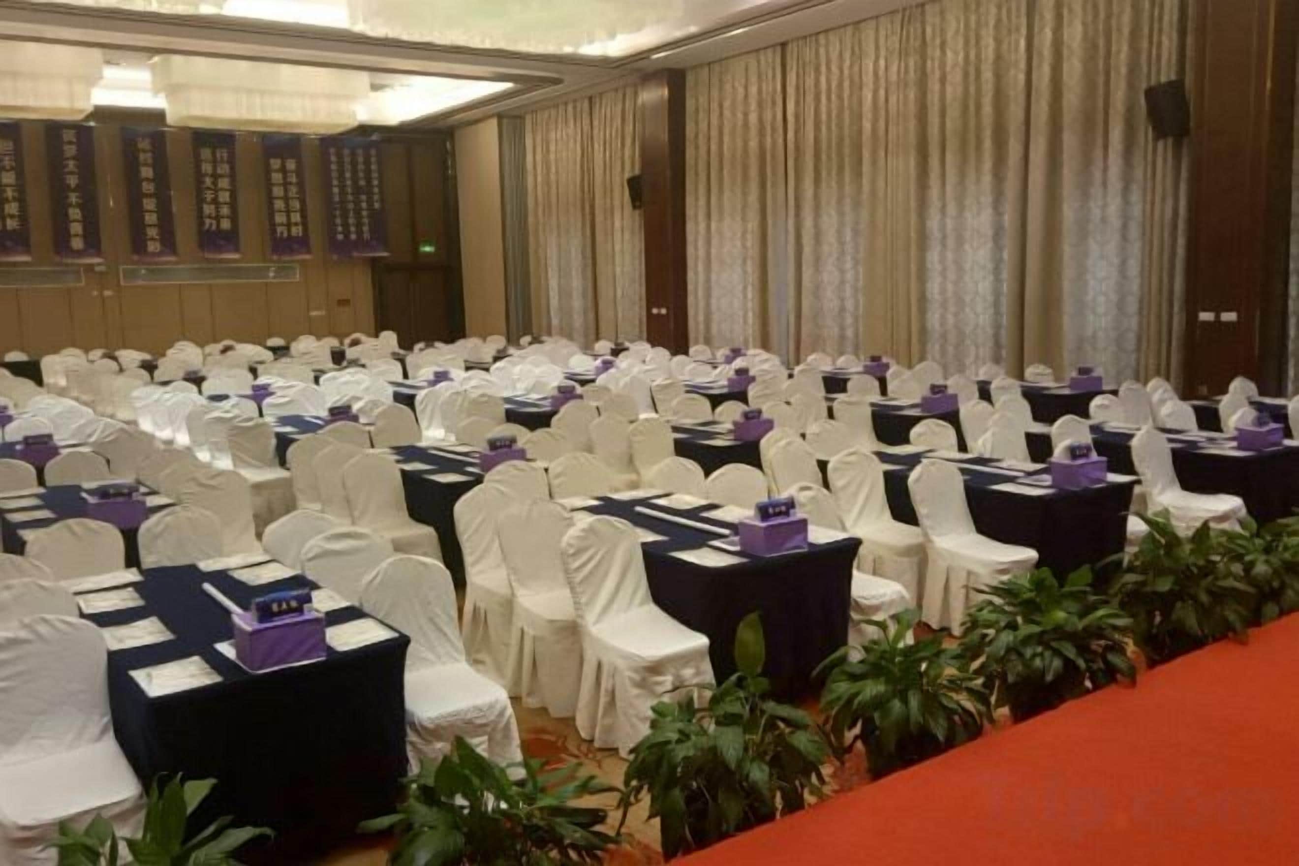 Un salón de conferencias con filas de mesas y sillas, algunas con centros de mesa morados.