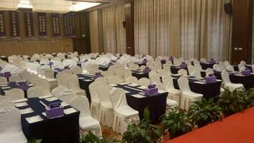 Un salón de conferencias con filas de mesas y sillas, algunas con centros de mesa morados.