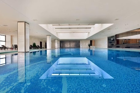 An indoor swimming pool with clear water, a central diving platform, and a modern architectural design.. Shenghe Regent Hotel