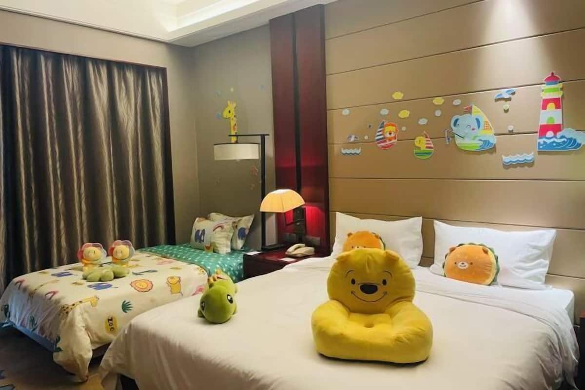 Quarto de hotel com duas camas, brinquedos macios, uma luminária e decorações nas paredes.