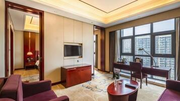A hotel room with a large window, a flat-screen TV, a desk, and a seating area.