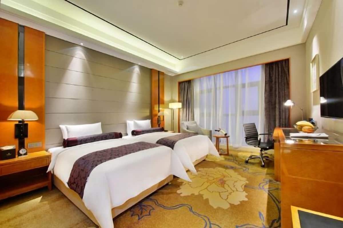Quarto de hotel com duas camas, uma escrivaninha, uma cadeira, uma televisão e uma janela com cortinas.