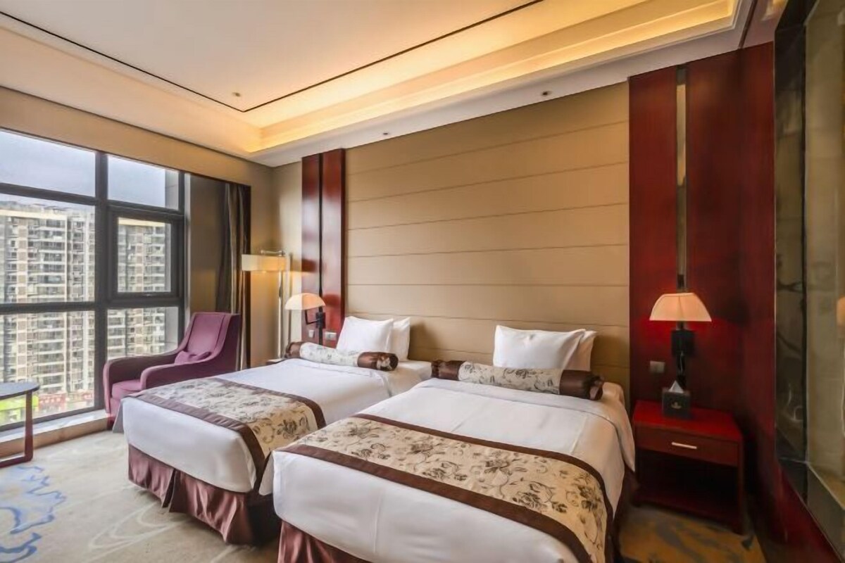 A hotel room with two beds, a large window, a chair, and a nightstand with a lamp.