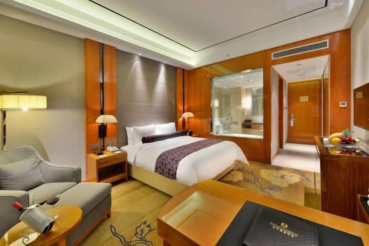 Quarto de hotel com cama, escrivaninha, cadeira, abajur e espelho.