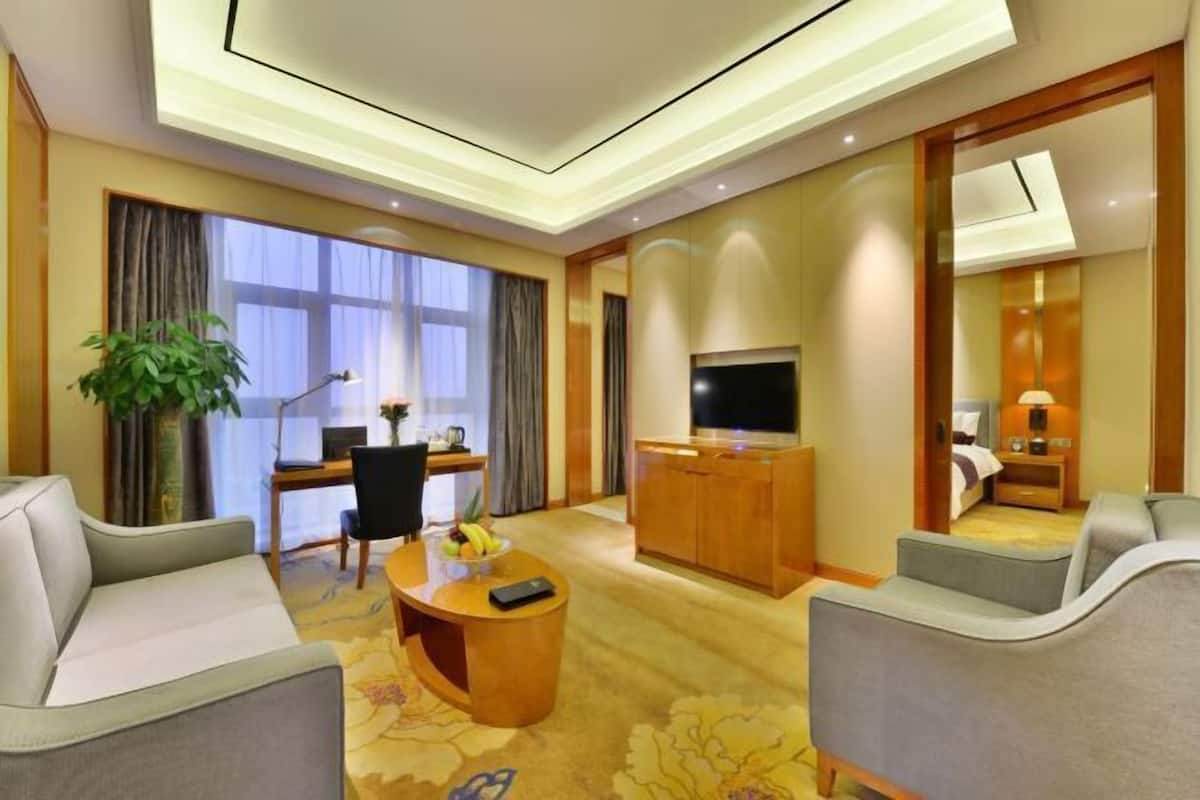 Quarto de hotel com sofá, secretária com computador, televisão e cama.