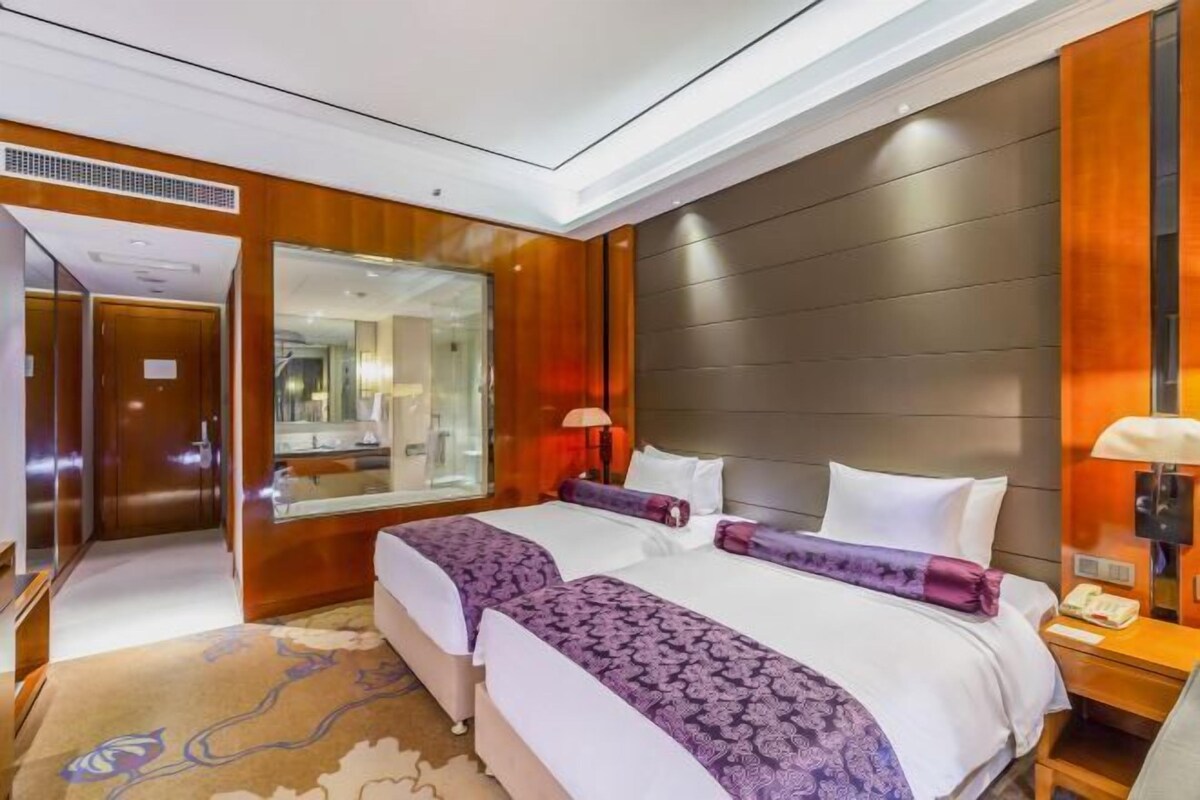 A hotel room with two beds, a large mirror, wooden paneling, and a nightstand with a lamp.