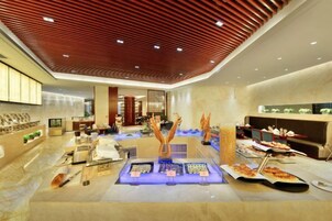 Un moderno vestíbulo de hotel con un mostrador de recepción central, una exhibición de joyería y un área de descanso con mesas.
