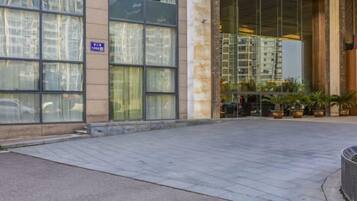 A building entrance with large windows, a paved area, and potted plants.