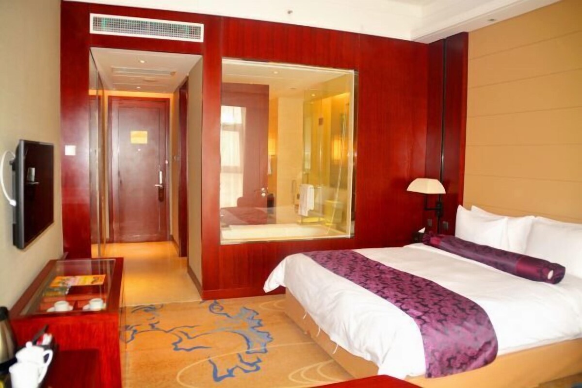 A hotel room with a bed, a TV, a desk with a chair, and a mirror.