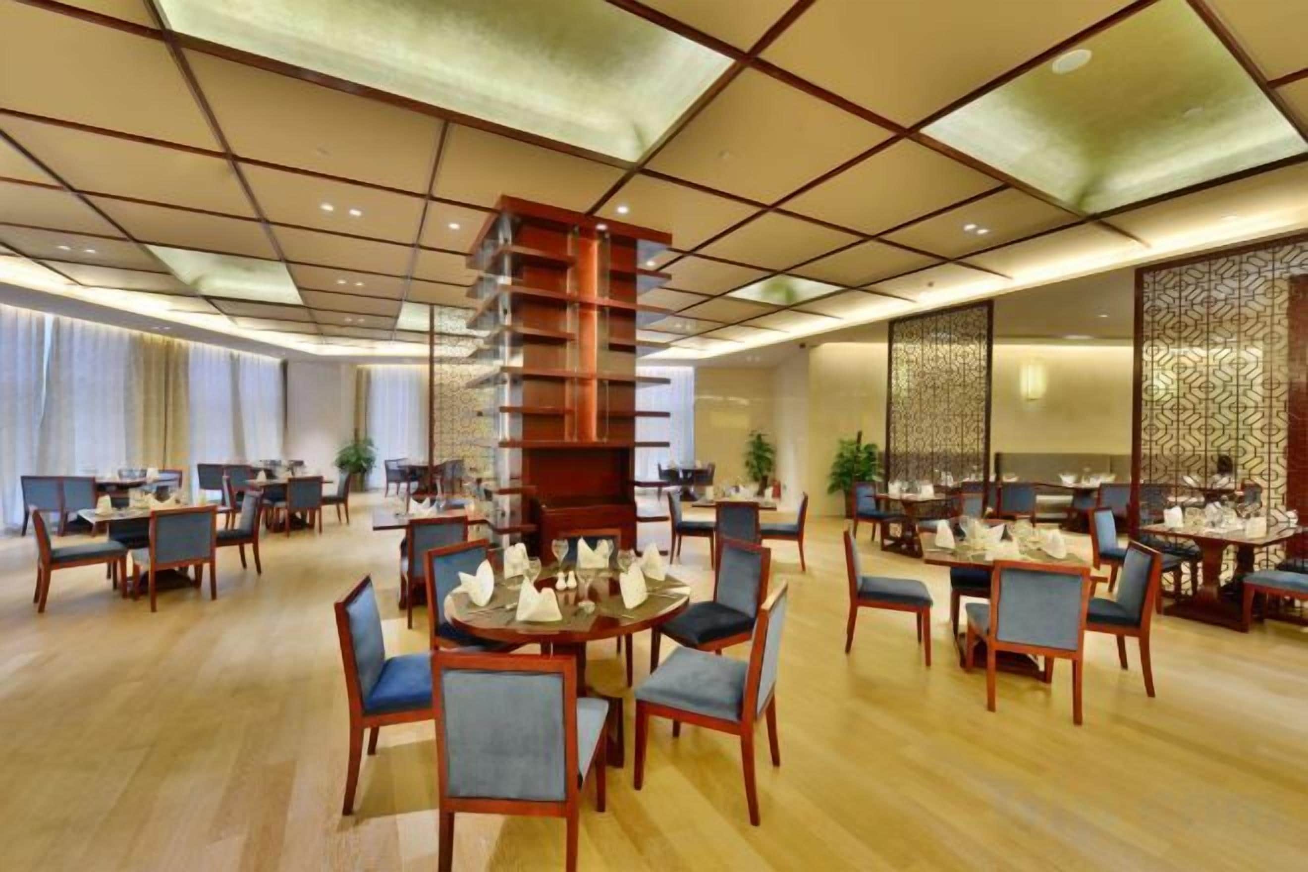A hotel dining area with multiple round tables, chairs, and a central decorative wooden structure.