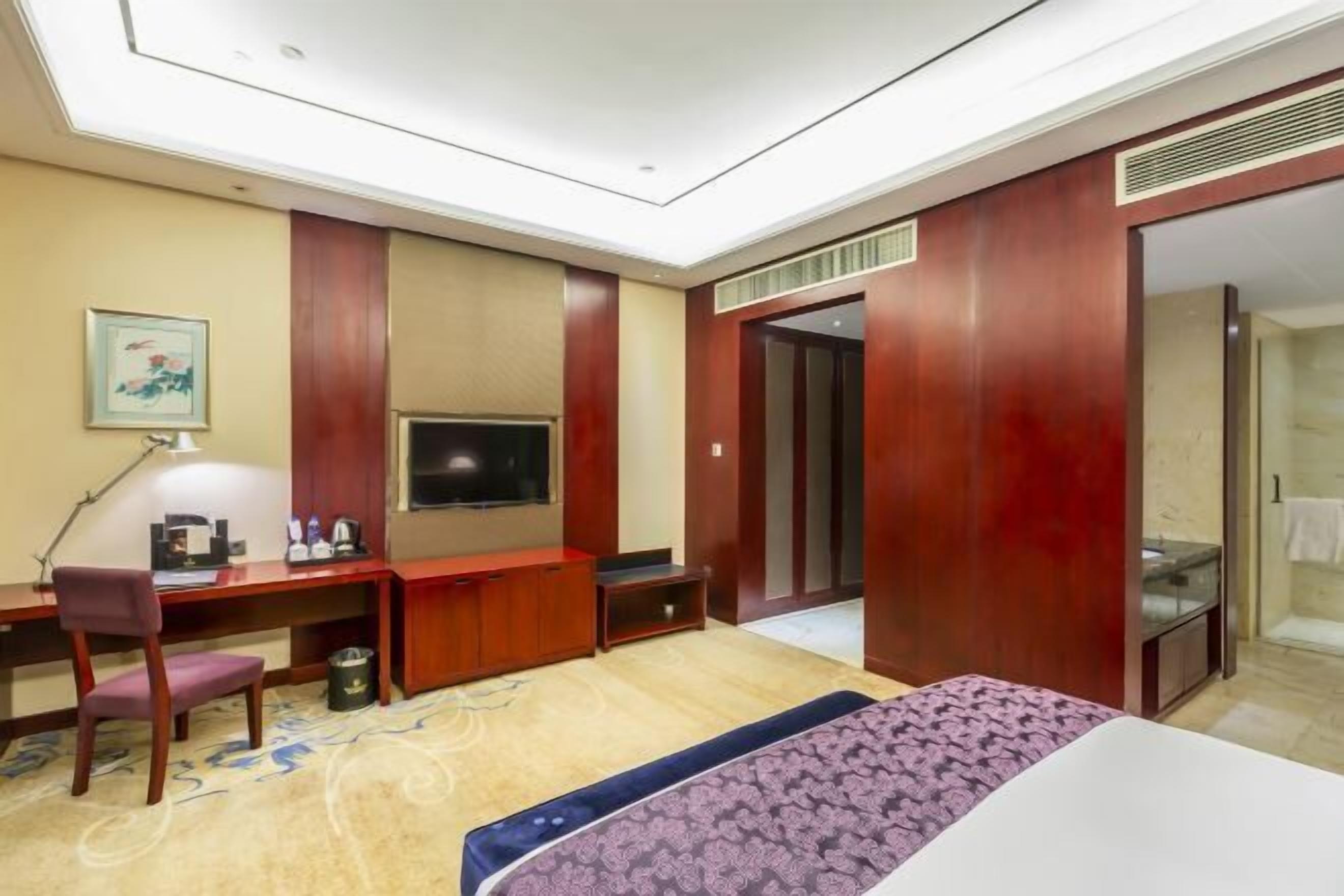 Ett hotellrum med en säng, ett skrivbord, en TV, en garderob och en duschhörna.