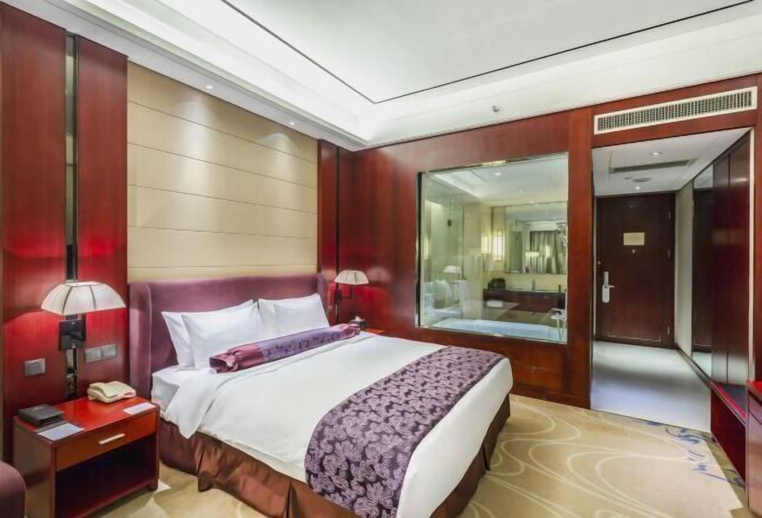 Una habitación de hotel con una cama grande, una mesita de noche, un espejo y una puerta que da a otra habitación.