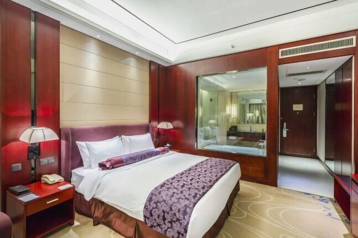 A hotel room with a large bed, a nightstand, a mirror, and a door leading to another room.