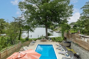 A backyard with a swimming pool, lounge chairs, and a view of a lake.
