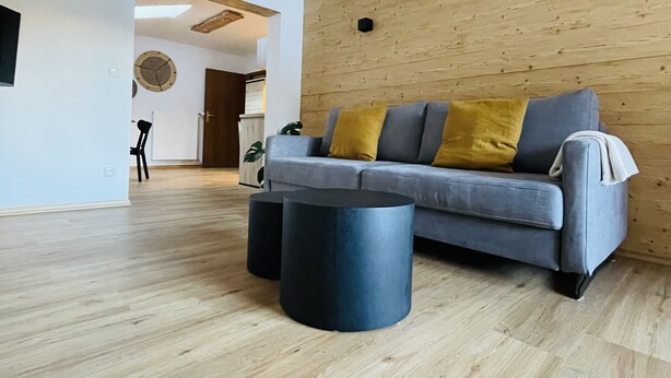 A modern living room with a grey sofa, wooden beams, a wooden wall, and a round coffee table.