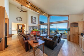A spacious living room with a fireplace, wooden ceiling beams, a large window overlooking the ocean, and a cozy seating area. - Sierra at Rubicon - 3 BR, Panoramic Lake Views, Private Hot Tub  HOA Private Beach! (Tahoma)