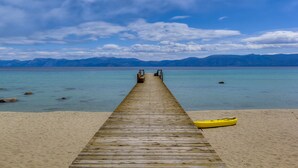 Une jetée en bois s’étendant sur une mer calme, avec un ciel dégagé et des montagnes en arrière-plan.