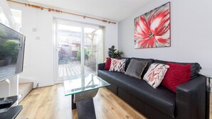 Un soggiorno moderno con un tavolino in vetro, un divano in pelle nera con cuscini decorativi, una televisione a schermo piatto e un grande quadro floreale appeso al muro.