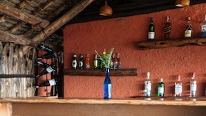 A rustic bar area with wooden stools and a shelf of liquor bottles. - Leopards Lair Cottages (Mtito Andei)