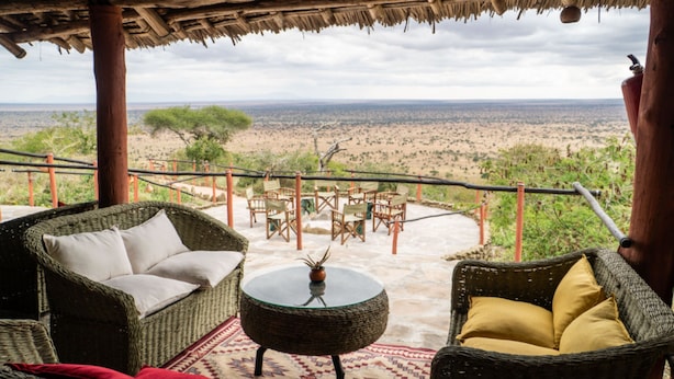 A wicker lounge area with a round table and chairs, overlooking a vast landscape. - Leopards Lair Cottages (Mtito Andei)