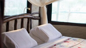 A bed with white linens and a floral-patterned bedspread, positioned against a window with sheer curtains. - Leopards Lair Cottages (Mtito Andei)