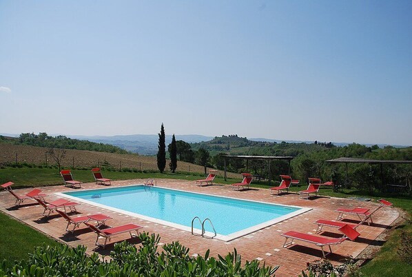 Une piscine rectangulaire entourée de chaises longues rouges, le tout se fondant dans un paysage de collines et d’arbres.
