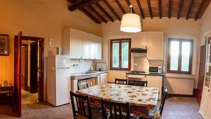 A cozy kitchen with white cabinets, a dining table with a sunflower tablecloth, and a hanging light fixture. - Casa Cassiodoro A: A characteristic age-old farm house surrounded by vineyards and olive groves, with Free WI-FI. (Castelfiorentino)