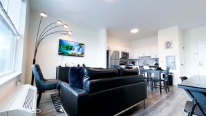 A modern living room with a black leather sofa, a flat-screen TV, and a dining area with a table and chairs. - ★Black & White Themed| 1BD/1BA|Parking★ (Bound Brook)