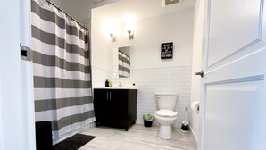 A modern bathroom with a striped shower curtain, a black vanity, a white toilet, and a small potted plant. - ★Black & White Themed| 1BD/1BA|Parking★ (Bound Brook)