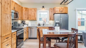 A kitchen with wooden cabinets, stainless steel appliances, a dining table with chairs, and a window. - Game Room & Wraparound Decks: Cullowhee Home! (Cullowhee)