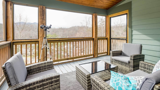 A covered outdoor area with wicker furniture, a tripod, and a view of the outdoors. - Game Room & Wraparound Decks: Cullowhee Home! (Cullowhee)