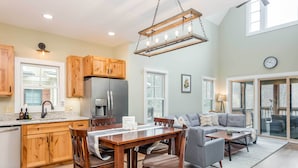 A spacious kitchen with wooden cabinets, a dining area with a table and chairs, and a living room with a gray sofa and a coffee table. - Game Room & Wraparound Decks: Cullowhee Home! (Cullowhee)