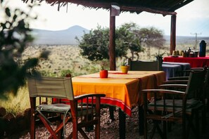 Un área de comedor al aire libre con mesas y sillas, un techo de paja y vistas del paisaje.