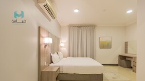Una habitación de hotel moderna con una cama grande, una mesita de noche de madera, un escritorio y un ventanal con cortinas.